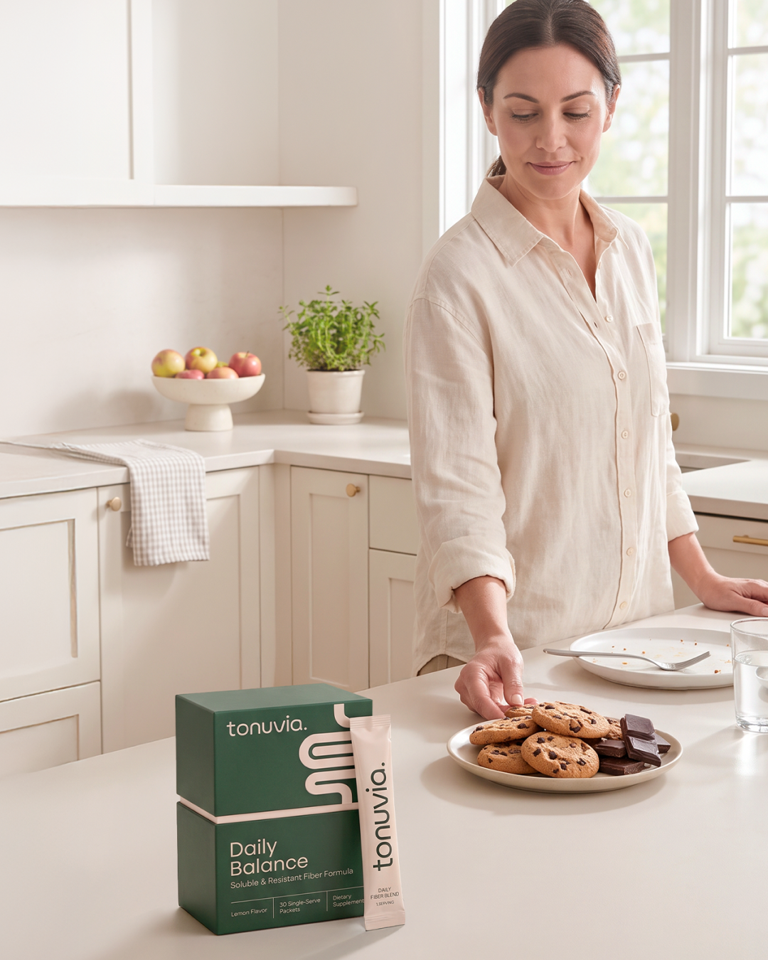 A woman in her kitchen beside dinner plates, cookies and Tonuvia Daily Balance.